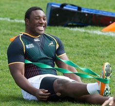 a rugby player sitting on the ground with a green ribbon around his ankles and smiling