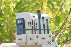 an assortment of pens and pencils are in a holder on a table outside near some trees