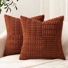 two brown pillows sitting on top of a white couch next to a potted plant