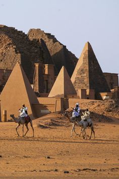 two men riding on the backs of camels in front of pyramids