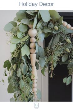 a wreath with wooden beads and greenery hanging from it's side on a door