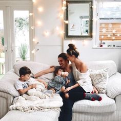 a woman and two boys sitting on a couch with lights strung above them in the background