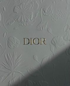 the word dior written in gold letters on a white wall with floral designs and leaves