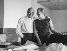 a man and woman standing next to each other in front of a bed with sheets on it