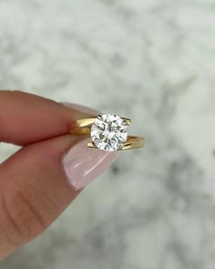 a woman's hand holding an engagement ring with a diamond in the middle, on a marble surface