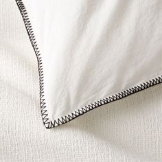 an unmade bed with white sheets and black piping on the pillowcases