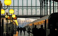 people are walking in the train station with their trains on tracks and lights hanging from the ceiling