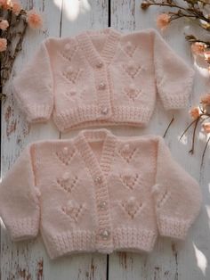 two pink knitted sweaters sitting on top of a white wooden table next to flowers