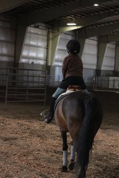 a woman riding on the back of a brown horse in an indoor arena at night