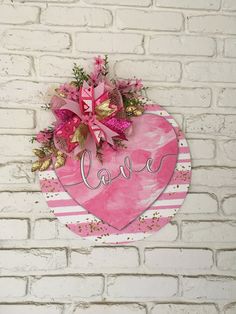 a heart shaped sign with pink flowers hanging on a white brick wall that says love