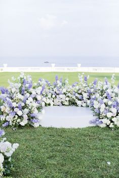 a white and blue wedding arch with flowers on the grass in front of an ocean