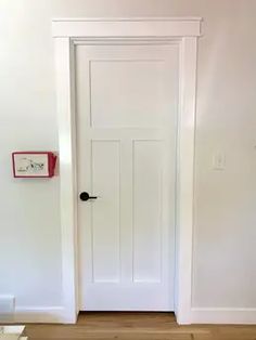 an empty room with a white door and wooden floors in front of the door is a clock on the wall