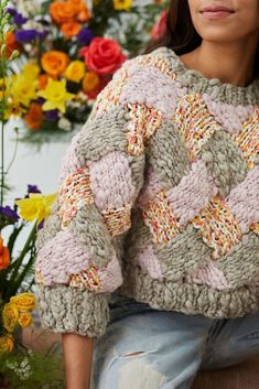 a woman sitting in front of flowers wearing a sweater with crochet patterns on it