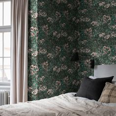 a bed sitting next to a window in a room with green wallpaper and white curtains