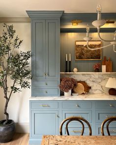 a kitchen with blue cabinetry and marble counter tops, an olive tree in the center