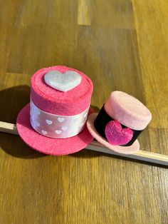 two hats are sitting next to each other on a wooden table, one has a pink hat with white polka dots and the other has a heart