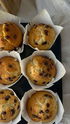 six muffins sitting in paper cups on a black tray with white napkins