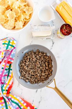 ingredients to make an appetizer laid out on a marble counter top, including tortilla chips and salsa