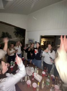 a group of people standing around a wooden table with drinks on it and one person holding up their hands in the air