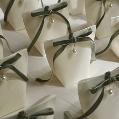 small white boxes with green ribbons and pearls on them are sitting on a tablecloth