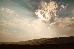 the sun shines through clouds in the sky over a desert landscape with hills and grass