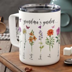 a white coffee mug with flowers and butterflies on it sitting next to marshmallows