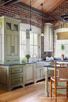 a kitchen with brick walls and wooden floors is pictured in this image, there are two chairs at the center of the room