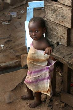 a small child in a towel standing next to a wooden bench and looking at the camera