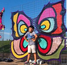 a young boy standing in front of a colorful butterfly made out of crochet