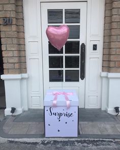 a pink heart shaped balloon sitting on top of a box in front of a door