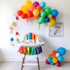 a baby's high chair in front of a wall decorated with balloons and streamers