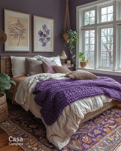 a bed with purple blankets and pillows in a bedroom next to a large potted plant