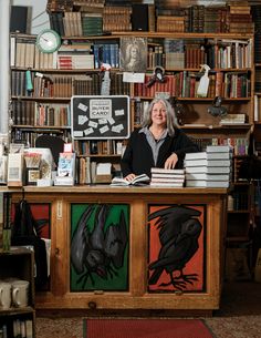 a woman sitting at a desk in front of bookshelves with paintings on it