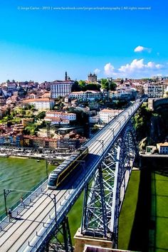 the train is going over the bridge on the water's edge in front of cityscape