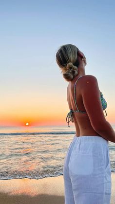 a woman standing on top of a sandy beach next to the ocean at sunset or sunrise