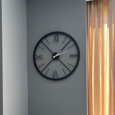 a clock on the wall with roman numerals is shown in front of a window