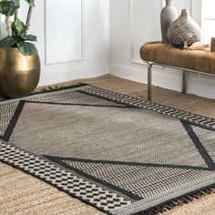 an area rug with black and white designs on it in front of a bench, potted plant and window