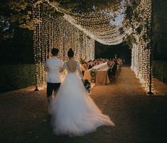 a bride and groom walking down the aisle at their outdoor wedding ceremony with fairy lights