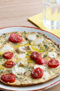 a pizza with tomatoes and mozzarella is on a plate next to a glass of water