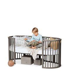 a small child sitting in a metal crib reading a book