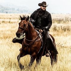 a man riding on the back of a brown horse across a dry grass covered field