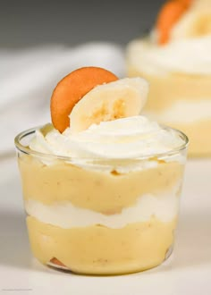 two desserts with banana slices and whipped cream in small glass dishes on a table