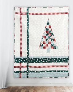 a quilted christmas tree hanging on the wall next to a wooden floor in front of a white wall