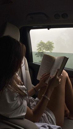 a woman sitting in the back seat of a car reading a book