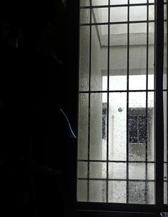 an open window with bars on it and rain coming in from the outside, behind which is a white door