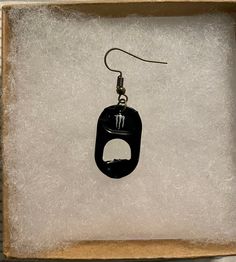 a pair of black earrings in a box with white paper on the bottom and silver earwires hanging from it