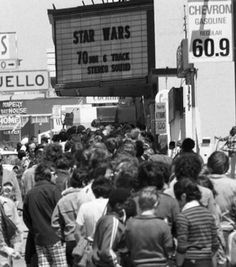 a crowd of people standing on the side of a road next to a movie marquee