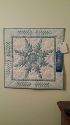 a blue and white quilt hanging on the wall next to a wooden table with a tag