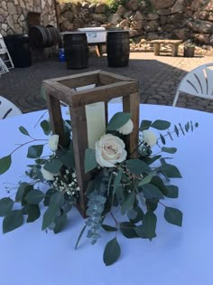 a candle holder with flowers and greenery on a blue table cloth at an outdoor event