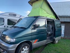 a van with a tent on the roof parked next to another van in a field